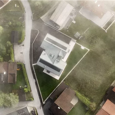 A modern house with a well-maintained garden, surrounded by other residential buildings. The shot is from a bird's eye perspective and shows a quiet neighborhood.