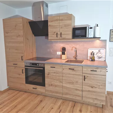 Eine moderne Küche aus Holz mit einer Arbeitsplatte und einem Herd. Sie verfügt über einen Kühlschrank und eine Mikrowelle sowie eine elegante Spüle.