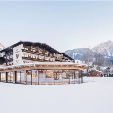 A modern hotel in the mountains, surrounded by snow and majestic peaks. The architecture is appealing and inviting.