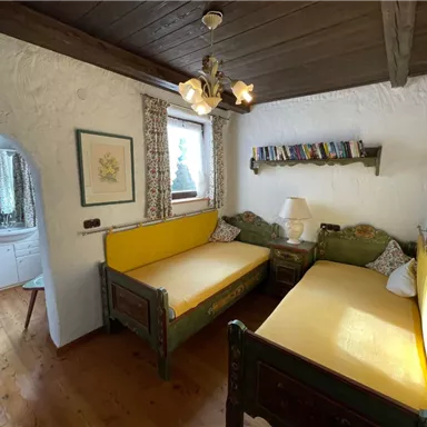 A cozy bedroom with two single beds and yellow mattresses. The room has wooden flooring and a view of the bathroom.