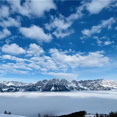 Eine atemberaubende Berglandschaft mit schneebedeckten Gipfeln und einem tiefblauen Himmel. Nebel bedeckt das Tal und verleiht der Szene eine mystische Atmosphäre.