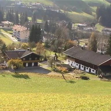 Ein malerisches Tal mit zwei traditionellen Bauernhäusern. Umgeben von Wiesen und sanften Hügeln, erstrecken sich Wälder im Hintergrund.