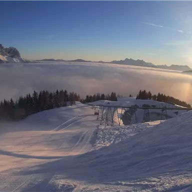 A beautiful snowy mountain overlooking clouds and the surrounding peaks. The sun rises, creating a picturesque atmosphere.