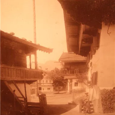 Eine schmaler Weg zwischen traditionellen Holzhäusern in einer malerischen Umgebung. Die warme Farbgebung verleiht dem Bild eine nostalgische Atmosphäre.