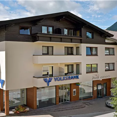 A modern building with a bank branch on the ground floor. In the background, mountains and a blue sky can be seen.