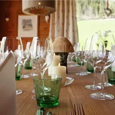Ein schön gedeckter Tisch mit Gläsern und Servietten. Im Hintergrund sind Fenster mit Blick ins Grüne und ein sanftes Licht.
