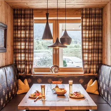 Ein gemütlicher Gastraum mit Holzinterieur und großen Fenstern. Auf dem Tisch stehen Getränke und eine kleine Auswahl an Speisen.