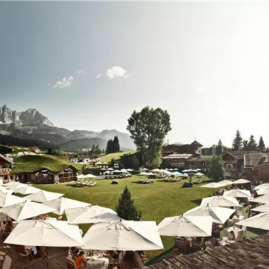 Ein schönes Hotel mit einem großen Garten und Sonnenschirmen. Im Hintergrund sind Berge und ein klarer Himmel zu sehen.