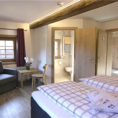 A cozy bedroom with two beds and a seating area. The adjoining bathrooms and windows create a bright atmosphere.