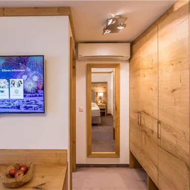 Ein modernes Zimmer mit Holzvertäfelungen und einem großen Fernseher. Am Ende des Flurs ist ein Spiegel zu sehen, der auf einen weiteren Raum hinweist.