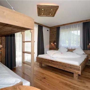 Ein gemütliches Zimmer mit Holzmöbeln und zwei Betten. Große Fenster lassen viel Licht herein und bieten einen Blick nach draußen.