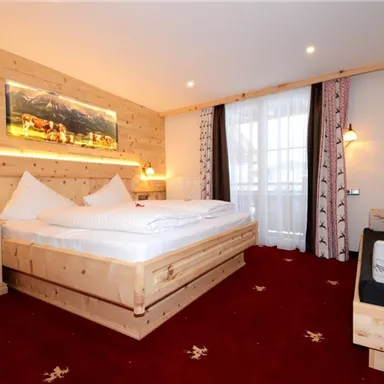 Ein gemütliches Hotelzimmer mit Holzverkleidung und einem großen Bett. Es gibt Fenster mit Vorhängen und einen bequemen Sessel.