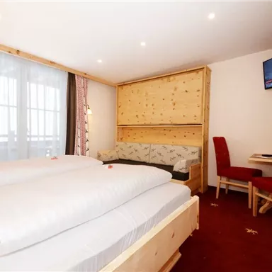 Ein modernes Schlafzimmer mit zwei Betten und einem bequemen Sitzbereich. Der Raum verfügt über einen Fernseher und große Fenster, die für viel Licht sorgen.