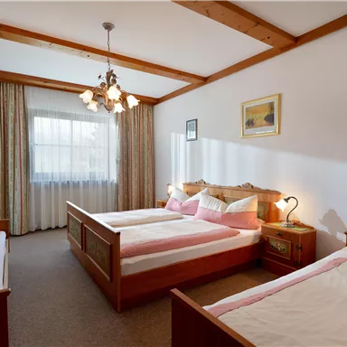 Ein gemütliches Schlafzimmer mit drei Betten und einem großen Fenster. Die Einrichtung ist hell und einladend, ideal für einen entspannten Aufenthalt.