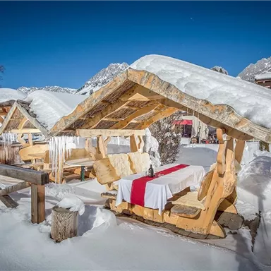 Ein schöner, schneebedeckter Außenbereich mit hölzernen Sitzgelegenheiten. Die Tische sind festlich gedeckt und von schmelzendem Schnee umgeben.