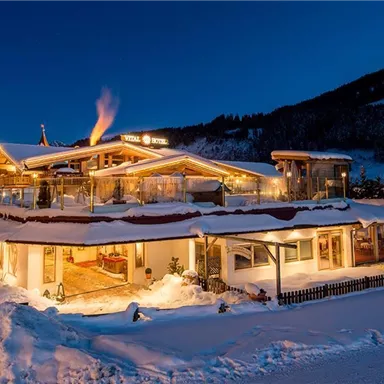 Ein gemütliches Gebäude im Schnee, festlich beleuchtet bei Nacht. Im Hintergrund sind schneebedeckte Berge zu sehen.