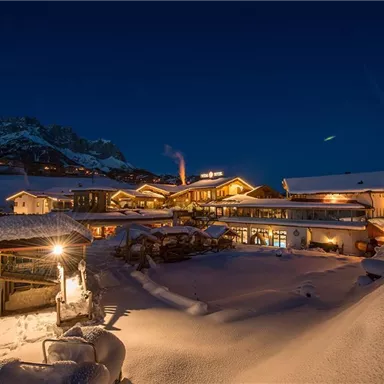 Ein malerisches Bergdorf bei Nacht, umgeben von schnee-covered Landschaft. Die beleuchteten Gebäude strahlen eine gemütliche Atmosphäre aus.