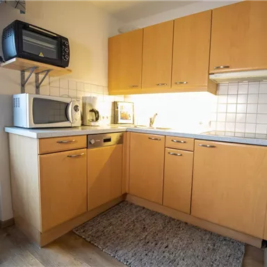 Eine moderne Küche mit hellen Holzschränken und weißen Fliesen. Es gibt eine Mikrowelle, einen Geschirrspüler und eine Kaffeemaschine.