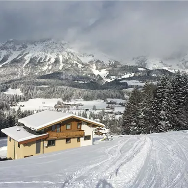 A modern house in a snow-covered landscape with impressive mountains in the background. The scenery conveys a calm winter atmosphere.