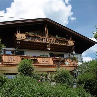 Ein traditionelles Haus mit einem großen Balkon und schönen Holzverzierungen. Umgeben von üppigem Grün und einem klaren Himmel.