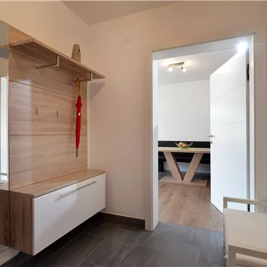 A modern hallway with a wooden frame and a white shoe cabinet. In the background, a table is visible that belongs to another room.