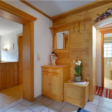 Ein gemütlicher Eingangsbereich mit holzverkleideten Wänden und einem kleinen Tisch mit Blumen. Der Raum hat eine warme, einladende Atmosphäre.