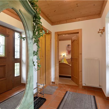 An inviting hallway with a large mirror and wooden details. The doors lead to additional rooms, and there are mats on the floor.