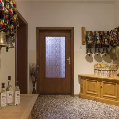 Ein gemütlicher Eingangsbereich mit Holzbank und dekorativen Glocken. Auf der Bank stehen Flaschen und ein Korb mit Obst.