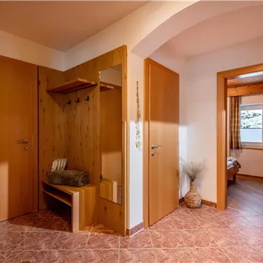 A bright hallway with wooden doors and a bench for sitting. On the left side are coat hooks and a small area with decorations.