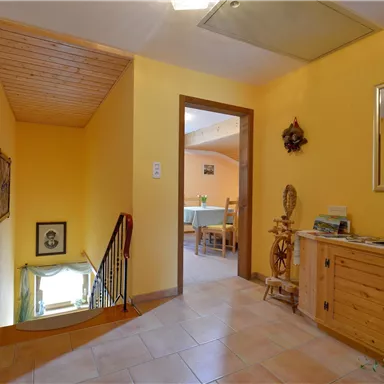 A bright hallway with yellow walls and a staircase. On the right side, there is a wooden dresser and in the background, you can see a dining area.