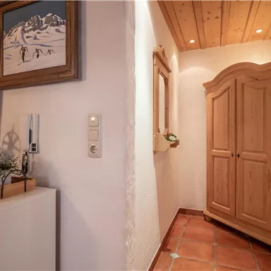 A cozy hallway with a beautiful wooden cabinet and skis on the wall. The walls are light and the wooden ceiling adds a warm atmosphere.