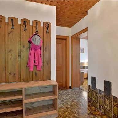 Ein Flur mit einem Holzkleiderständer und einer rosa Jacke hängt daran. Auf der rechten Seite sieht man eine Tür, die zu einem anderen Raum führt.