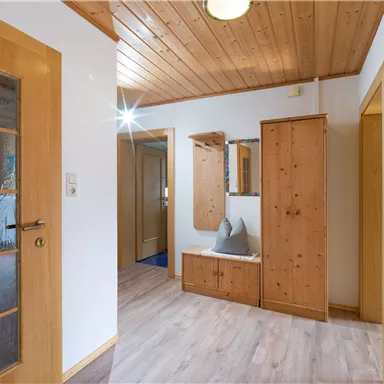 Ein heller Flur mit Holzwänden und einem Holzregal. Der Boden ist aus hellem Laminat und es gibt einen Spiegel an der Wand.