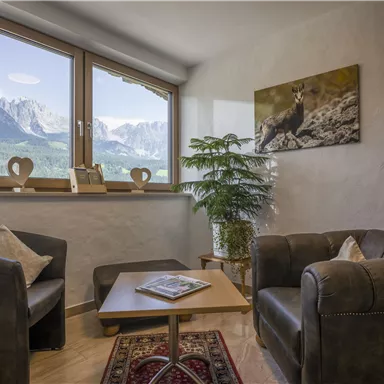 Ein gemütlicher Wohnraum mit zwei Sessel und einem Tisch. Große Fenster bieten einen Blick auf die Berge.