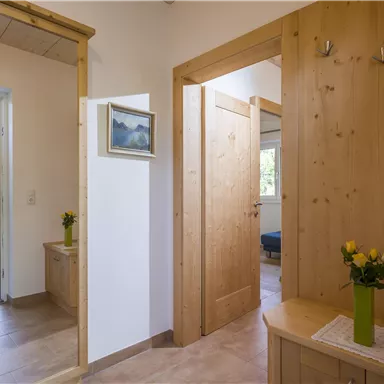 Ein heller Flur mit Holzwänden und Türen. Auf einem Tisch steht eine Vase mit gelben Blumen.
