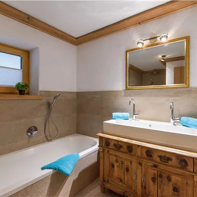 Ein modernes Badezimmer mit einer Badewanne und zwei Waschbecken. Holz- und Steinoberflächen sorgen für eine warme Atmosphäre.