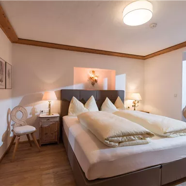 Ein gemütliches Schlafzimmer mit einem großen Doppelbett und hellen Kissen. Die warme Beleuchtung und die neutralen Farben schaffen eine einladende Atmosphäre.