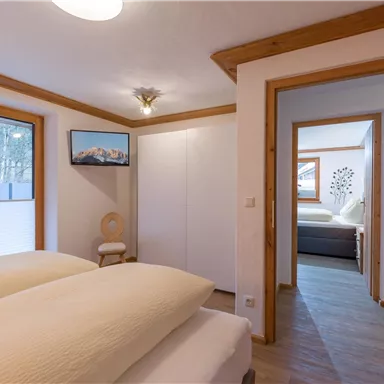 Ein modernes Schlafzimmer mit zwei Betten und großen Fenstern. Der Raum hat helle Wände und gemütliche Holzdetails.