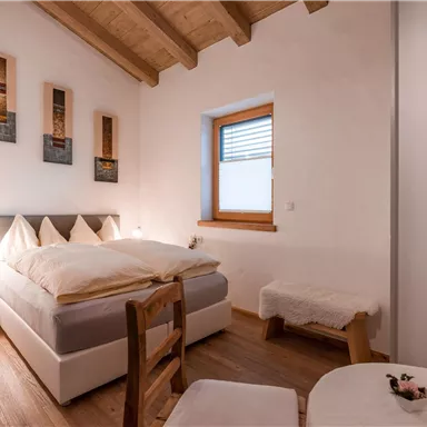 Ein gemütliches Schlafzimmer mit einem Doppelbett und heller Holzdecke. Die Wände sind schlicht und es gibt einen kleinen Tisch und Stühle.