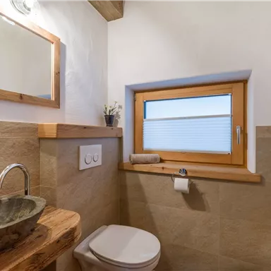 Ein modernes Badezimmer mit einer Steinwaschschüssel und Holzregalen. Das Fenster bringt Tageslicht in den Raum und sorgt für eine angenehme Atmosphäre.