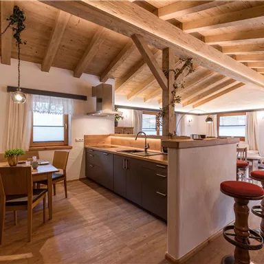 Eine moderne Küche mit Holzdecke und gemütlichem Essbereich. Die Einrichtung ist freundlich und hell, mit großen Fenstern für viel Tageslicht.