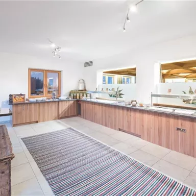 Ein modernes Frühstücksbuffet mit Holzregalen und einer großzügigen Theke. Helle Wände und natürliche Beleuchtung schaffen eine freundliche Atmosphäre.