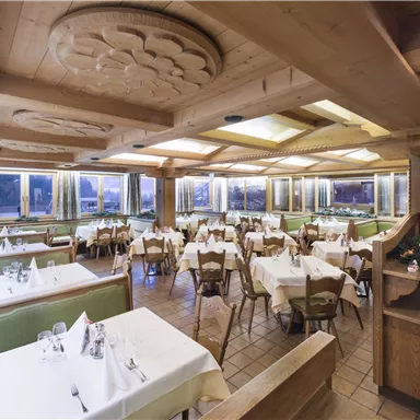 Ein gemütliches Restaurant mit Holzelementen und mehreren Tischen. Die Tische sind mit weißen Tischtüchern gedeckt und der Raum ist hell erleuchtet.
