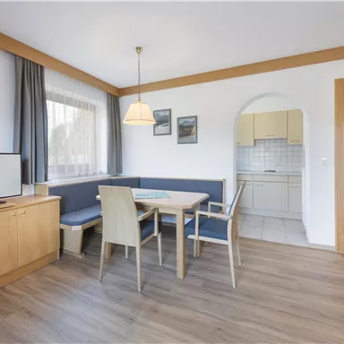 Ein gemütlicher Wohnraum mit einem Essbereich und einem Fernseher. Die Küche ist durch einen Bogen sichtbar und der Boden ist aus Holz.