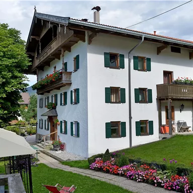 A charming white house with green shutters and a balcony. The garden is blooming and invites you to relax.