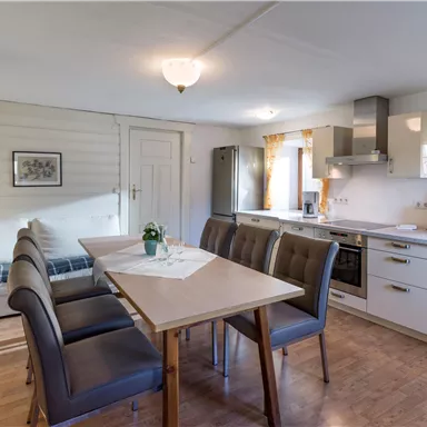 A modern kitchen with a dining area and a large table. Light walls and a wooden floor create an inviting atmosphere.