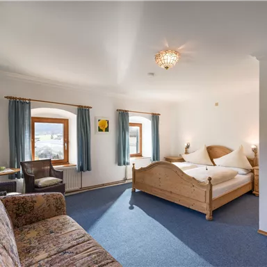 A comfortable room with a large bed and a cozy seating area. Bright windows create a friendly atmosphere.