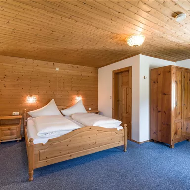 A simple bedroom with a wooden ceiling and wooden bedroom furniture. The room offers a double bed and a wardrobe in a cozy atmosphere.