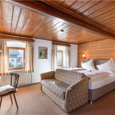 A cozy room with wooden walls and a double bed. There is a small table and a sofa area, perfect for relaxing.