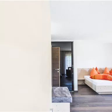 Ein modernes Schlafzimmer mit einem großen Bett und orangefarbenen Kissen. Die Wände sind hell und der Boden ist aus Holz.